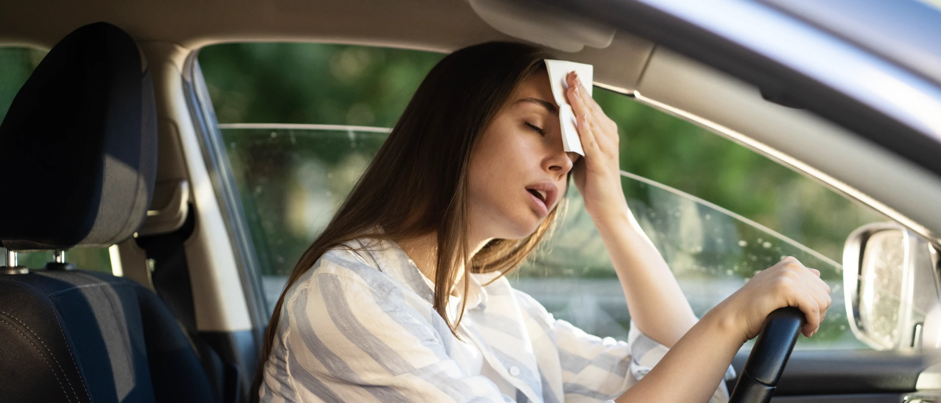 frau-im-auto-bei-sommerhitze-ohne-klimaanlage Frau sitzt im Auto bei offenem Fenster in der Sommerhitze ohne Klimaanlage